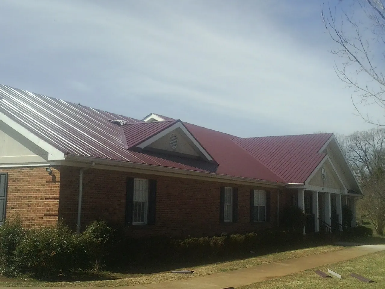 Red metal roof with gabled entries on a long brick building, from a Hail Damage Roof Repair job in Modena