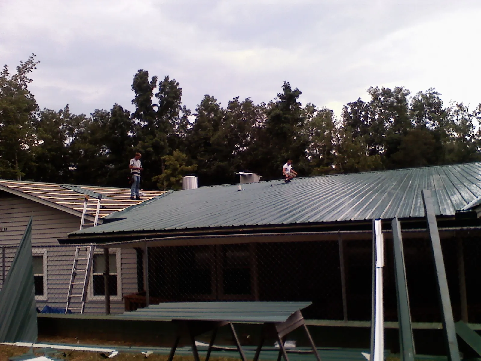 Two roofers installing green metal panels above a covered porch in Modena