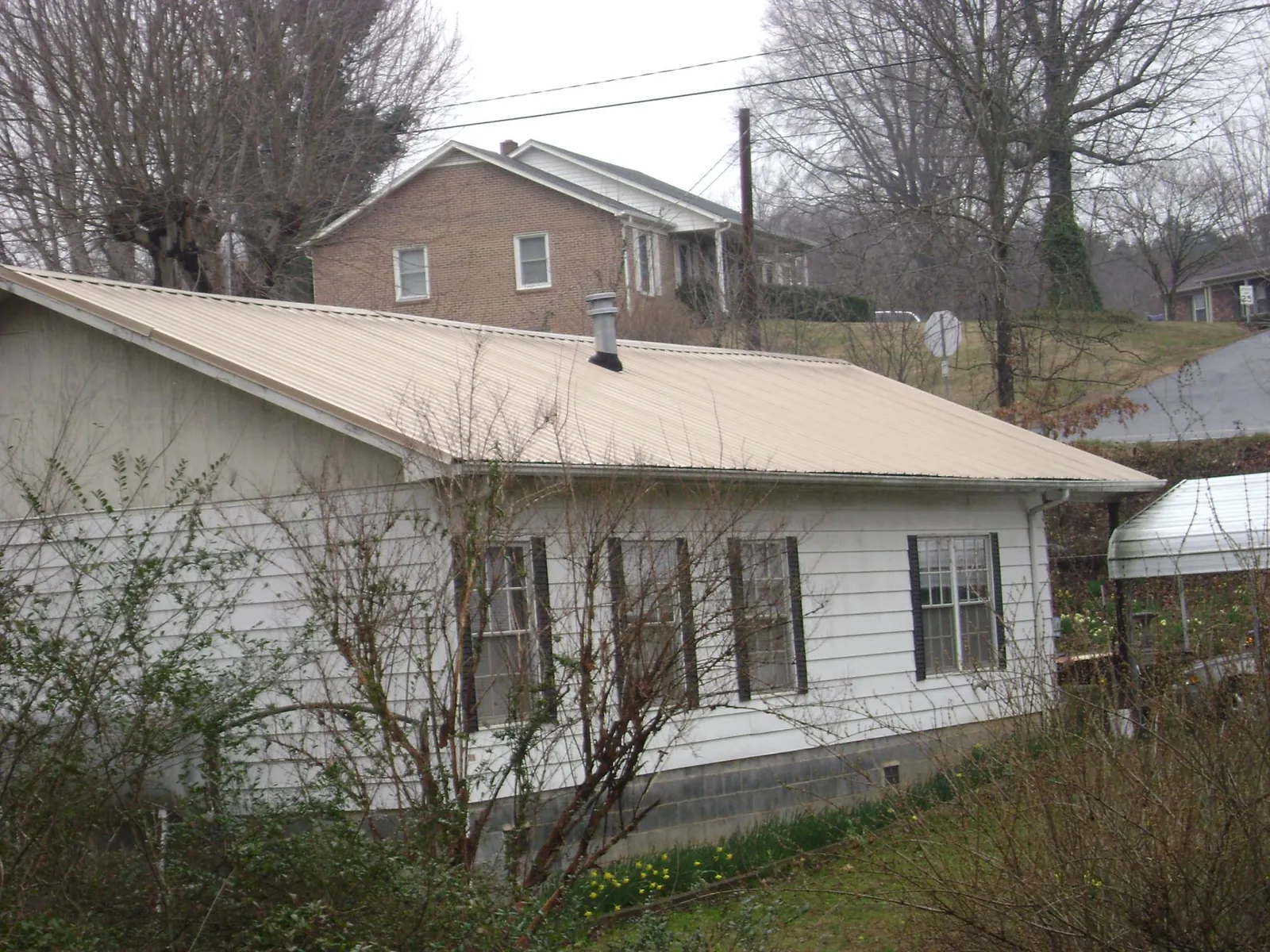 Tan metal roof on a white sided house set into a hillside — Commercial Roofing by Roofing Brothers in Modena